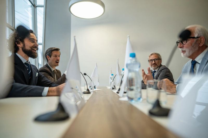 Group of diverse business professionals engaging in a serious discussion during a corporate meeting in a modern conference room, sharing ideas and strategizing future plans