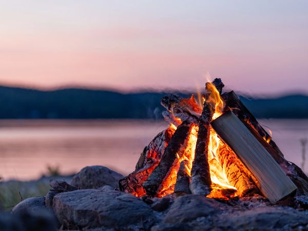 A campfire glowing by a lake at sunset.
