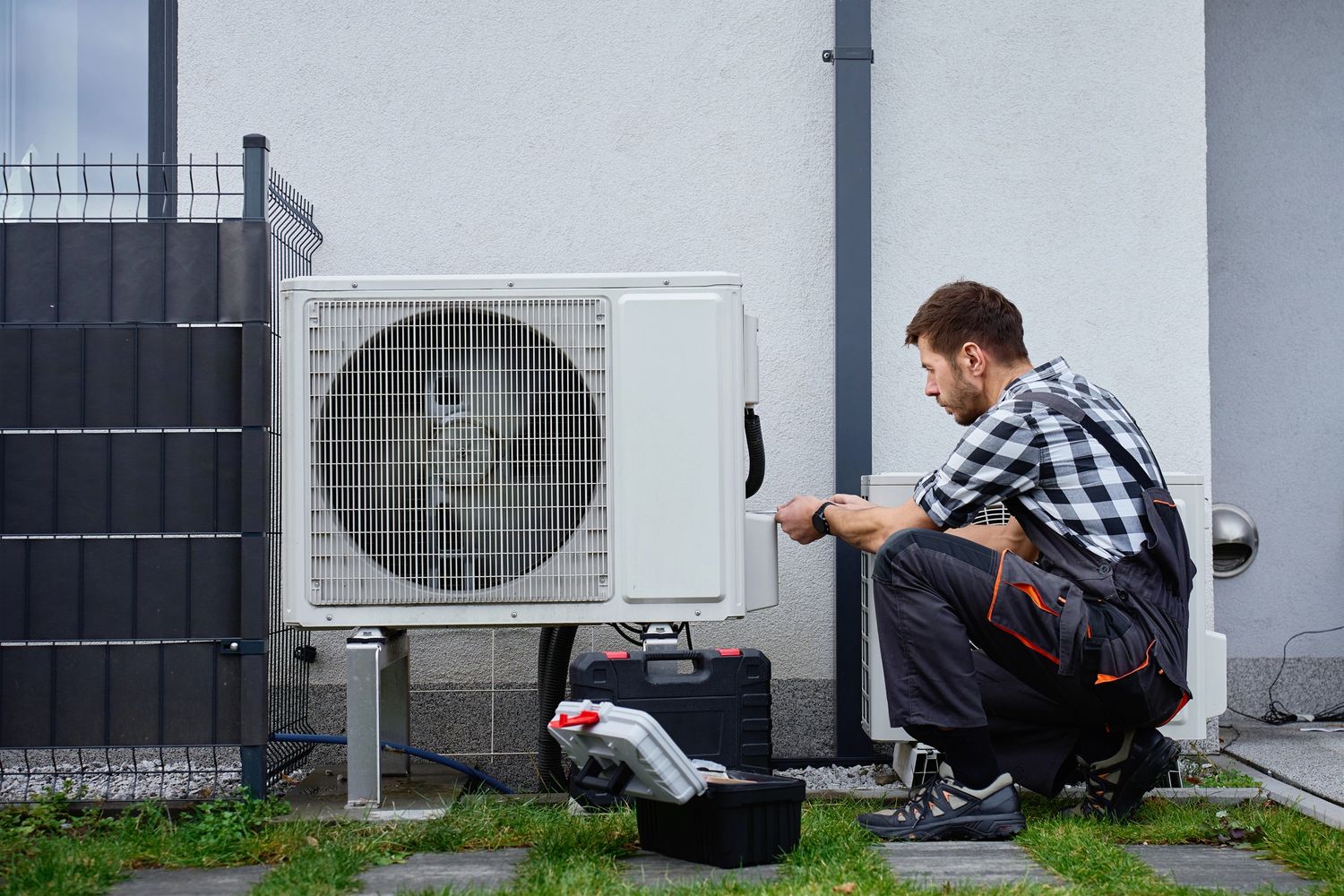 Technician repairing an outdoor air conditioning unit by a house.