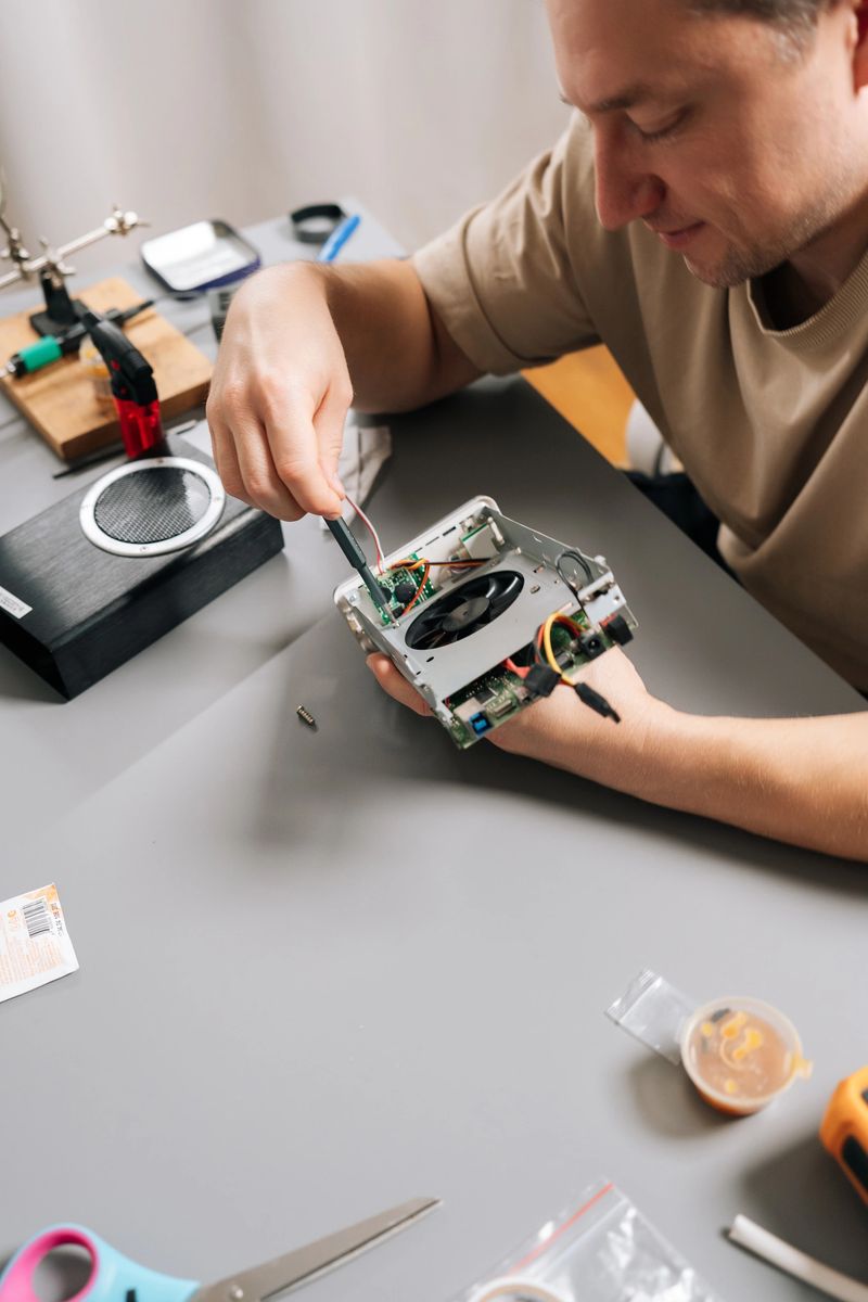 Top view of technician male working on electronic device, holding computer hardware with exposed cooling fan, performing repairs and maintenance on tech equipment in modern workshop.