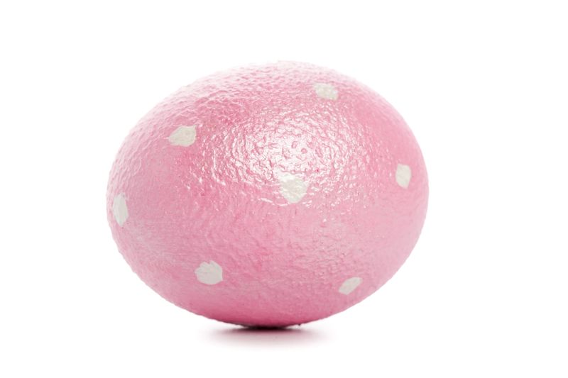 A round pink object sits on a white surface with small white dots visible on its surface.