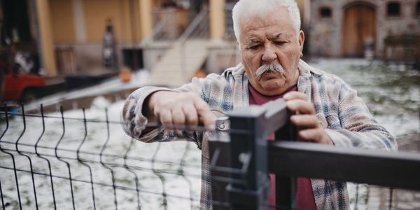 Elderly man fixing a metal fence outdoors with tools.