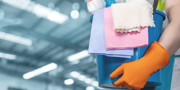 Person holding a cleaning bucket with gloves and cloths.