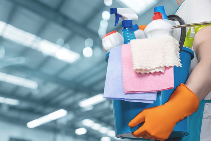 Sparkling space cleaning. A person in orange gloves carries a bucket of cleaning supplies indoors.