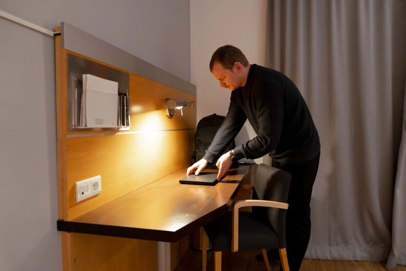 Man setting up his laptop on a desk in a hotel room for remote work