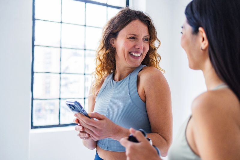 Two fit women share a smile and conversation during a gym session.