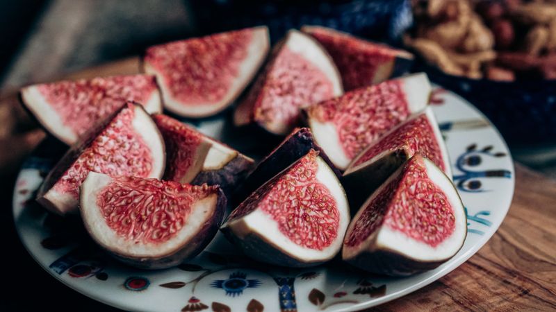 Quartered figs arranged on a decorative saucer with blue and red patterns. The deep reddish interiors contrast with the dark purple skin, highlighting the fruit’s natural richness and fiber-packed texture. The image blends visual pleasure with nutritional relevance, ideal for themes of healthy eating and culinary simplicity