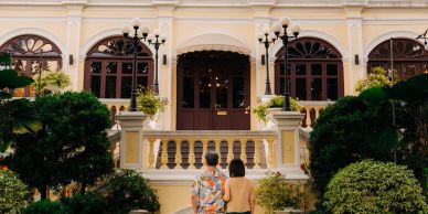 Two people standing in front of a grand entrance of a yellow building.