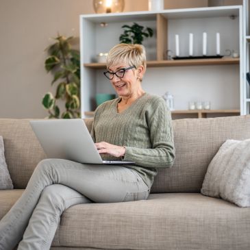 Smiling older woman using laptop on cozy couch.