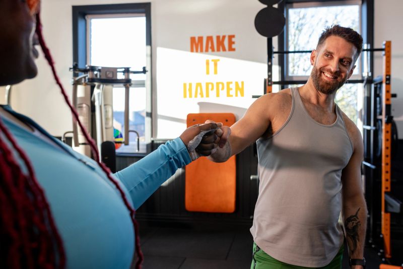 Over the shoulder shot of a personal trainer and client working out in a gym in Northumberland, North East England. They are fist bumping each other, celebrating a workout set together. Videos are available similar to this scenario.