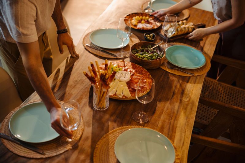 Close up of young couple is preparing an dinner setting. They are arranging plates, glasses, and decorations on a beautifully set table, smiling and enjoying the moment as they get ready to host friends. The atmosphere is warm and inviting, suggesting an evening of good food, conversation, and connection.