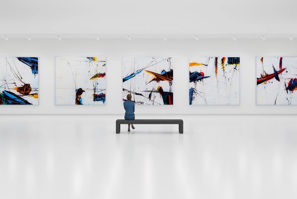 Person sitting on a bench observing abstract paintings in a modern gallery.