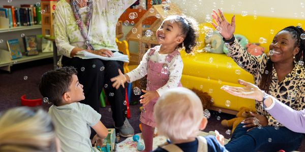 Children and adults joyfully playing with bubbles in a colorful room.