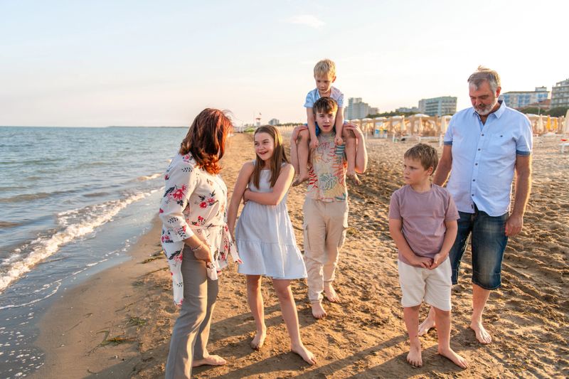 Family group walking together on a sandy beach, sharing laughter and stories. Children interacting playfully with grandparents, creating joyful memories by the sea under the evening sun.