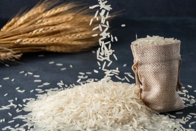 Rice grains spilling from a sack with wheat in the background.