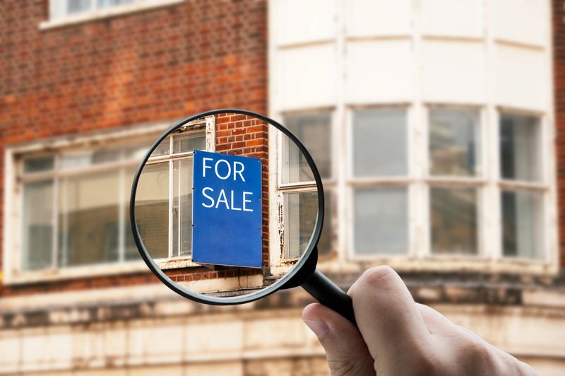 Magnifying glass focusing on a “For Sale” sign on a residential building. Concept of real estate and property market.