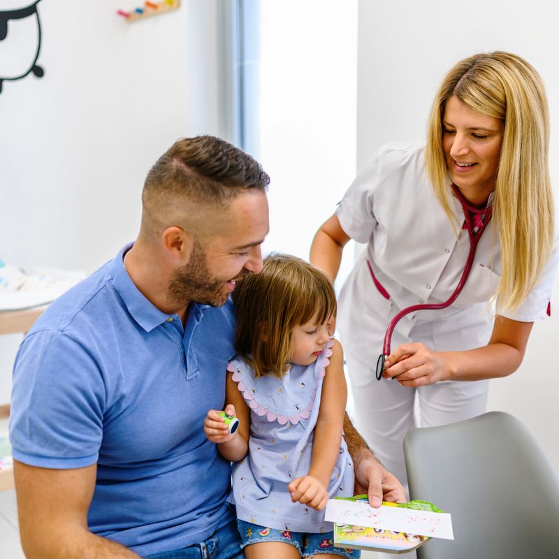 A toddler sits on his father's lap during a routine checkup