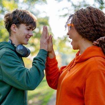 Two people smiling and giving a high five outdoors.