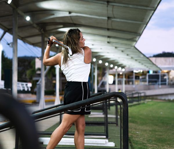 Woman practicing golf swing at a driving range during dusk.