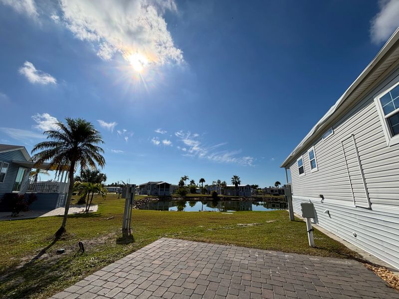 Canal front mobile homes in a residential community on Fort Myers Beach, Florida, featuring a bright sunny sky, green grass, and swaying palm trees reflecting on the water
