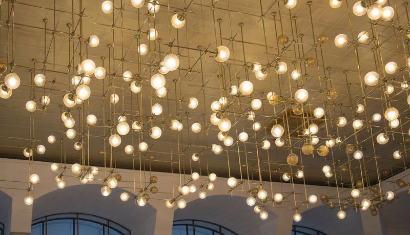 Modern ceiling light installation with suspended glowing glass spheres and geometric metal structure in elegant interior.