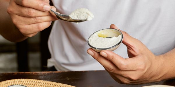Person scooping creamy white dip from a small bowl with a spoon.