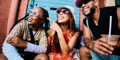 Three friends smiling and relaxing outdoors with drinks.