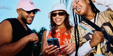 Three friends smiling and enjoying a moment looking at a phone outdoors.