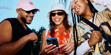 Three friends happily looking at a phone outdoors.