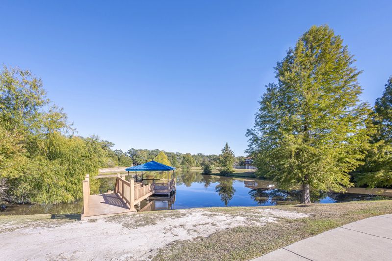 A wooden boardwalk and a cobalt-blue roofed gazebo overlook a tranquil artificial lagoon in a residential area of ​​the United States. An ideal spot for fishing, meditation, or simply enjoying nature.