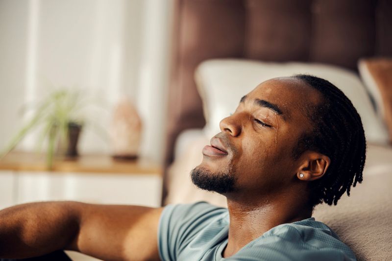 Young adult man relaxing on the floor at home, feeling tired and sweating after an intense fitness workout, demonstrating dedication and perseverance in his exercise routine