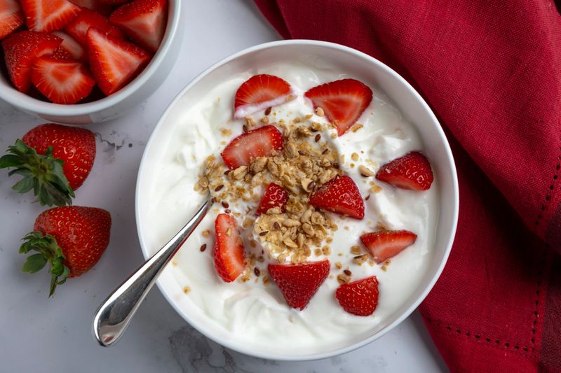 A bowl of creamy Greek yogurt topped with crunchy granola and fresh sliced strawberries
