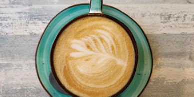 Top view of a latte with leaf latte art in a teal cup on a textured surface.