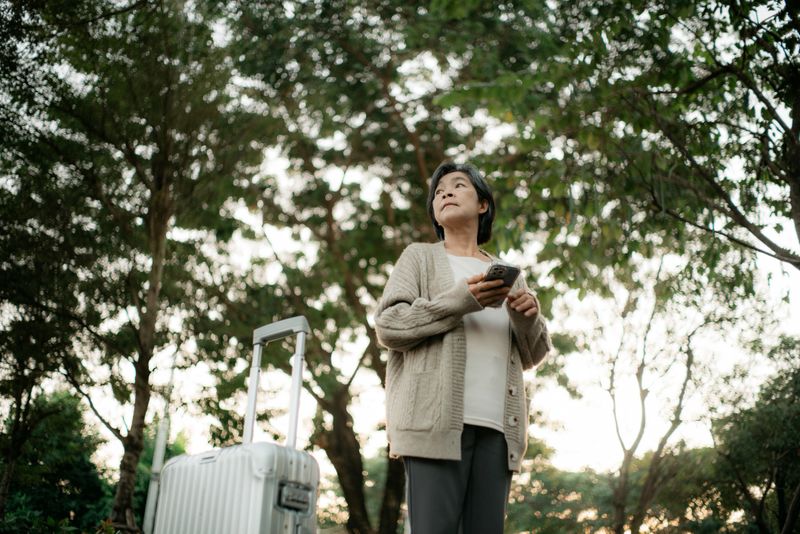Mature Asian businesswoman calling a taxi with a suitcase.