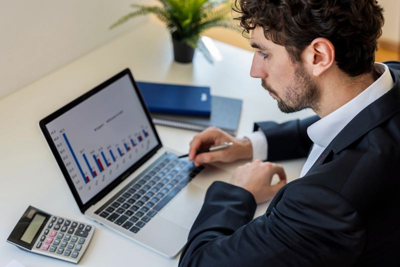 Focused businessman analyzing financial data and charts on a laptop computer at a modern workspace. Concept of business analysis, finance management, investment planning and professional decision making.