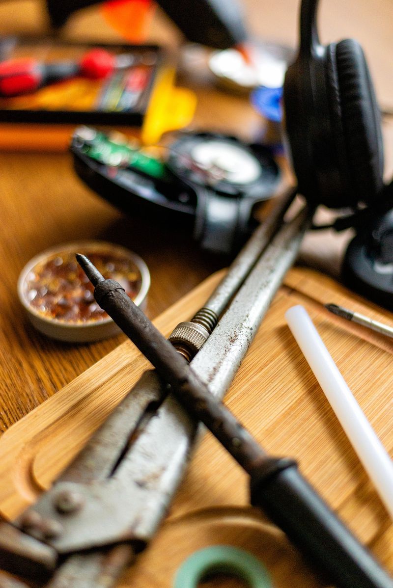 A collection of old and new hand tools, including pliers and a soldering iron, sitting on a wooden surface ready for a repair job.