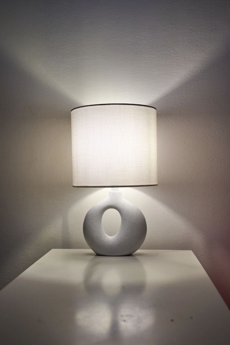 Symmetrical lamp reflection on glossy table, centered ceramic base and cylindrical shade create calm balanced