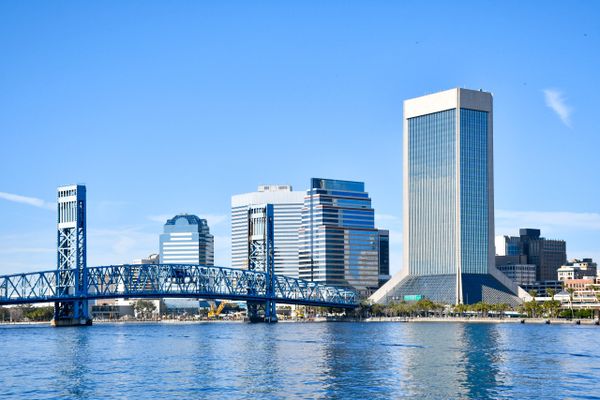 City skyline with a blue bridge over calm water on a clear day.