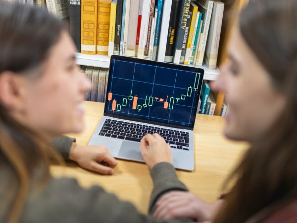 Two women analyzing stock charts on a laptop in a library.