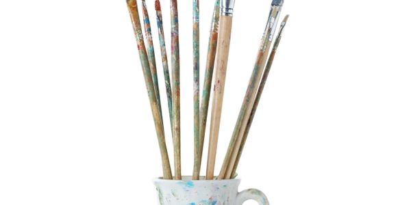 Paintbrushes in a paint-splattered ceramic cup.