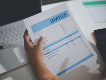 Person holding an invoice near a laptop.