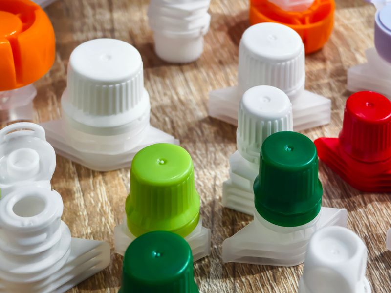 Multiple plastic bottle caps in various colors are spread across a wooden surface, showcasing their different shapes and designs against a natural backdrop.