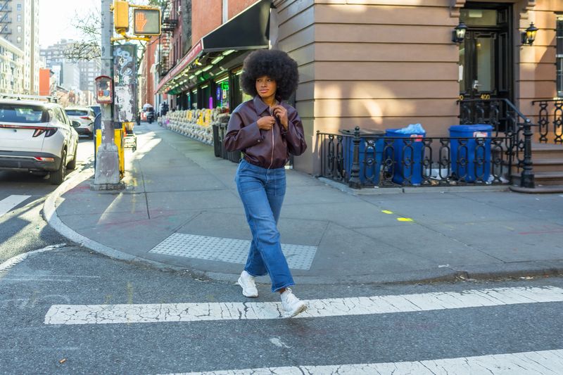 Young black woman with an afro hairstyle and street fashion crossing a pedestrian crosswalk in manhattan, new york city, creating an urban lifestyle and fashion concept