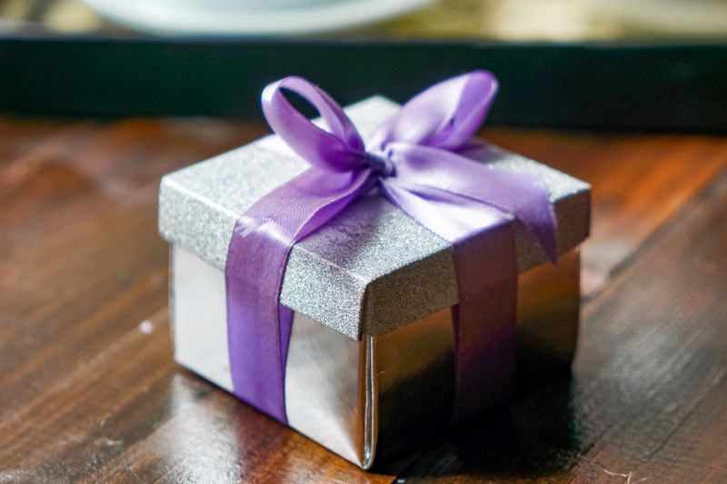 Sparkling silver gift box with lavender ribbon bow placed on rustic wooden tabletop