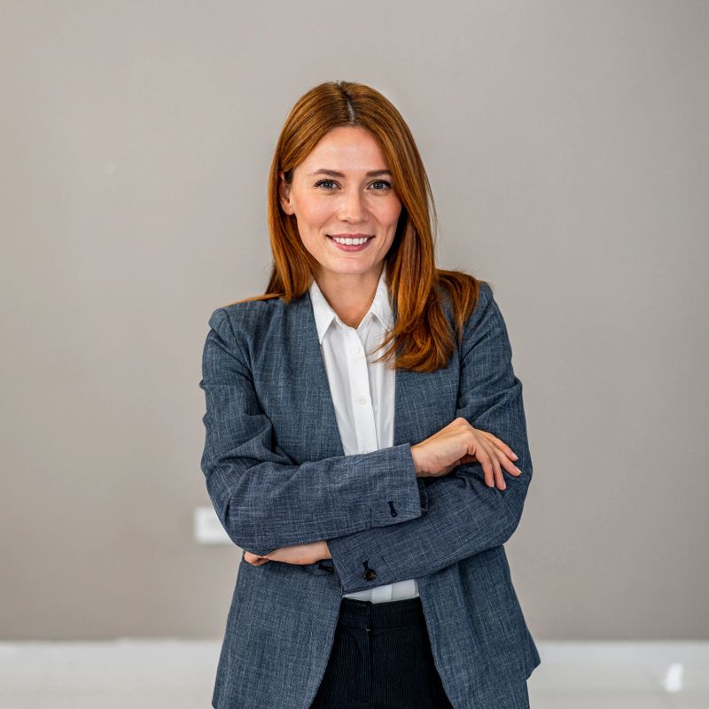 Professional young adult woman in a blazer and white shirt, smiling and standing with arms crossed, portraying leadership