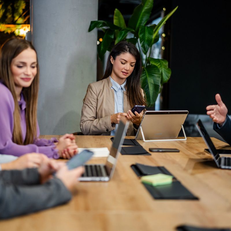 Business people attending a meeting, using laptops, tablets, and smartphones for collaboration in a modern office setup