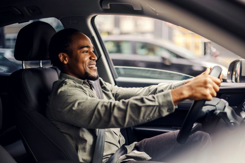 Young african-american man driving a car with a relaxed, confident smile during a daytime commute or road trip, enjoying independence, comfort and modern city travel