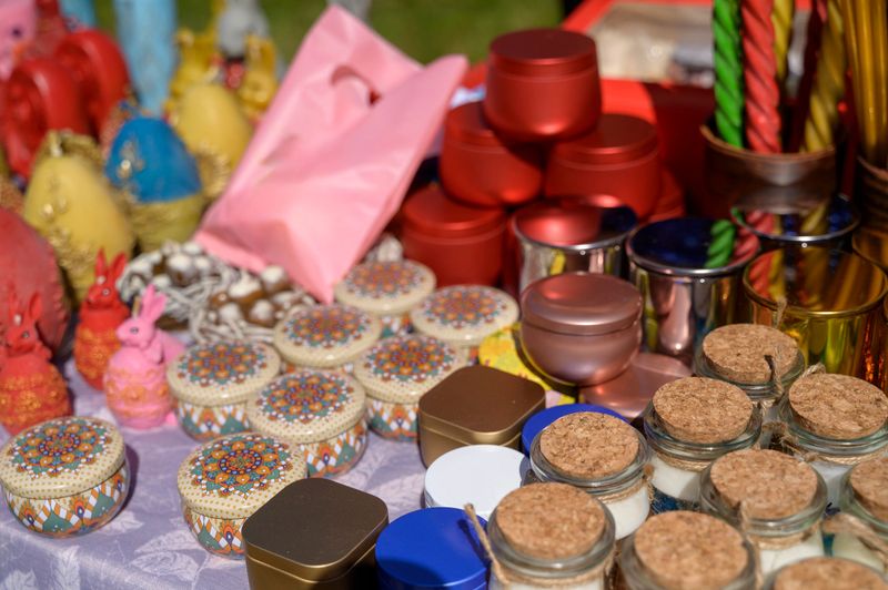 Display of colorful artisanal candles in metal tins and glass jars at a spring street fair in Europe. Concept of creative handmade gifts, home interior accessories, and market shopping