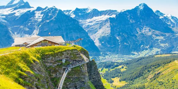 A scenic mountain lodge perched on a cliff with snowy peaks in the background.