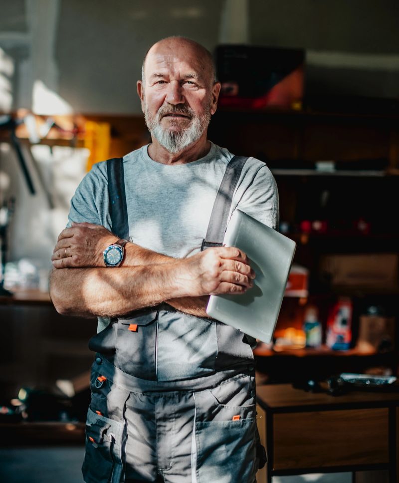 A handyman is in a workshop surrounded by tools and materials. He stands confidently with a tablet in his hands, ready to work on various projects.